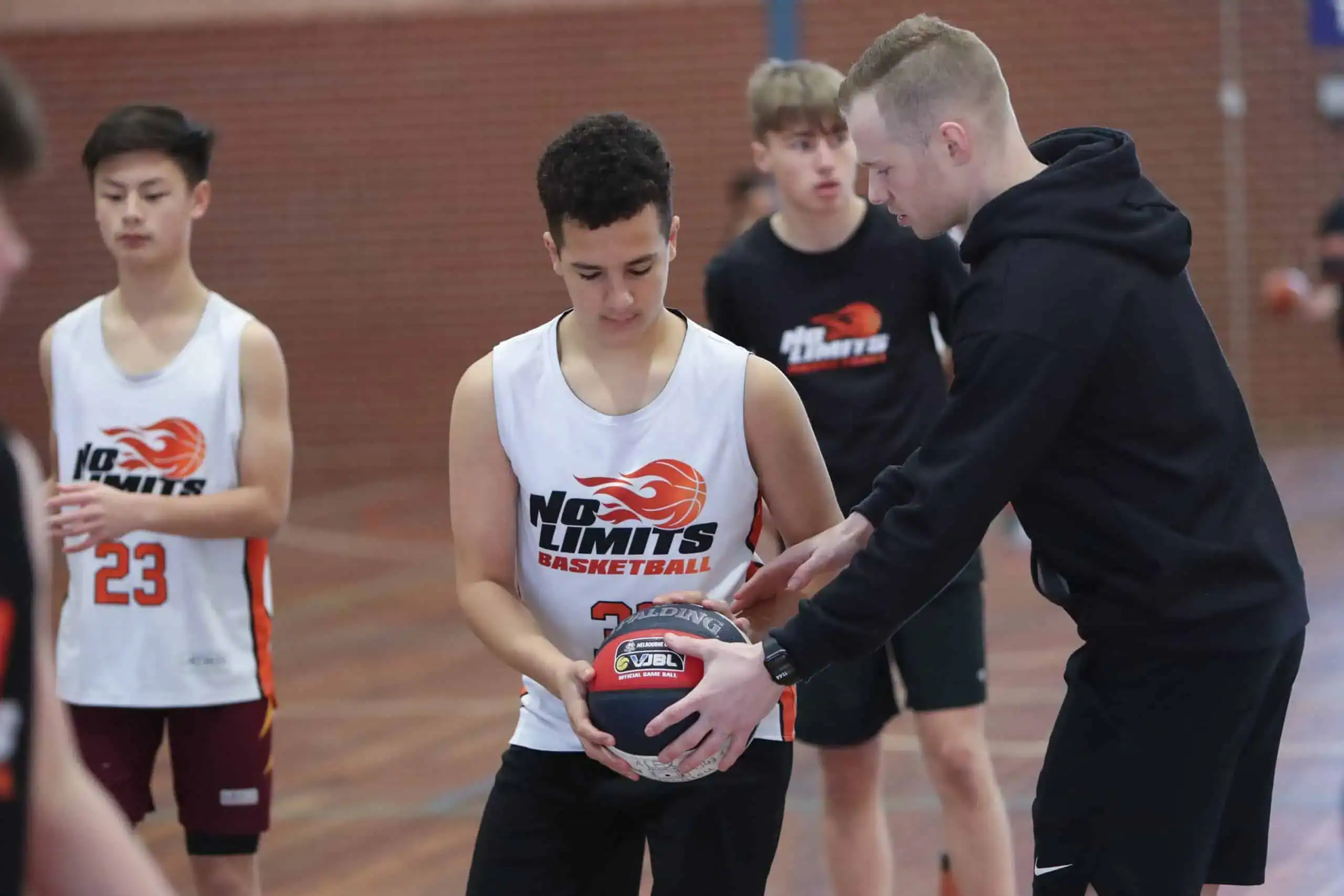 Young basketball players coaching and practicing skills during a No Limits Basketball training session in a gym.