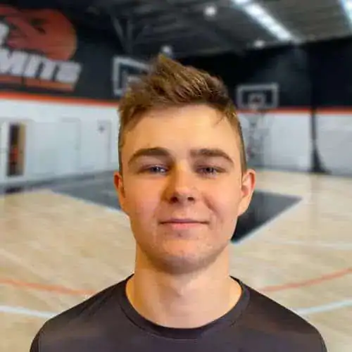 Young male basketball player in gym, smiling, indoor court background.