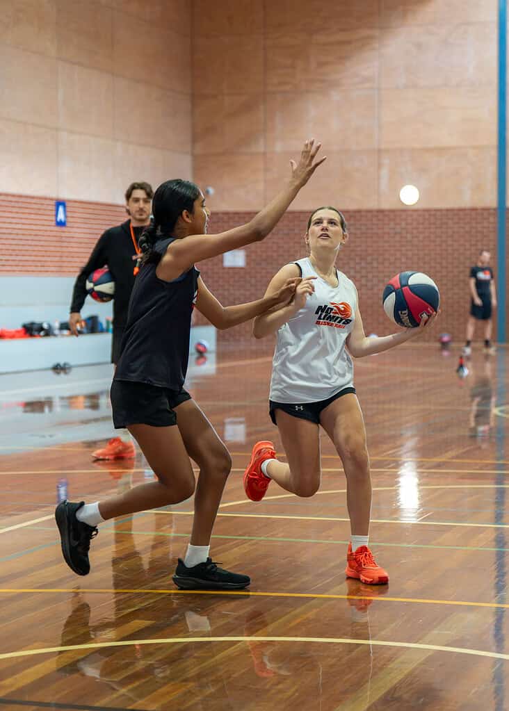 Women playing basketball in indoor court during training session.