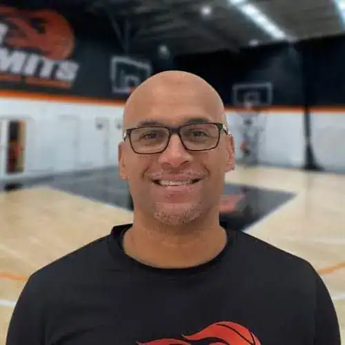 Smiling basketball coach in gym with basketball court background.