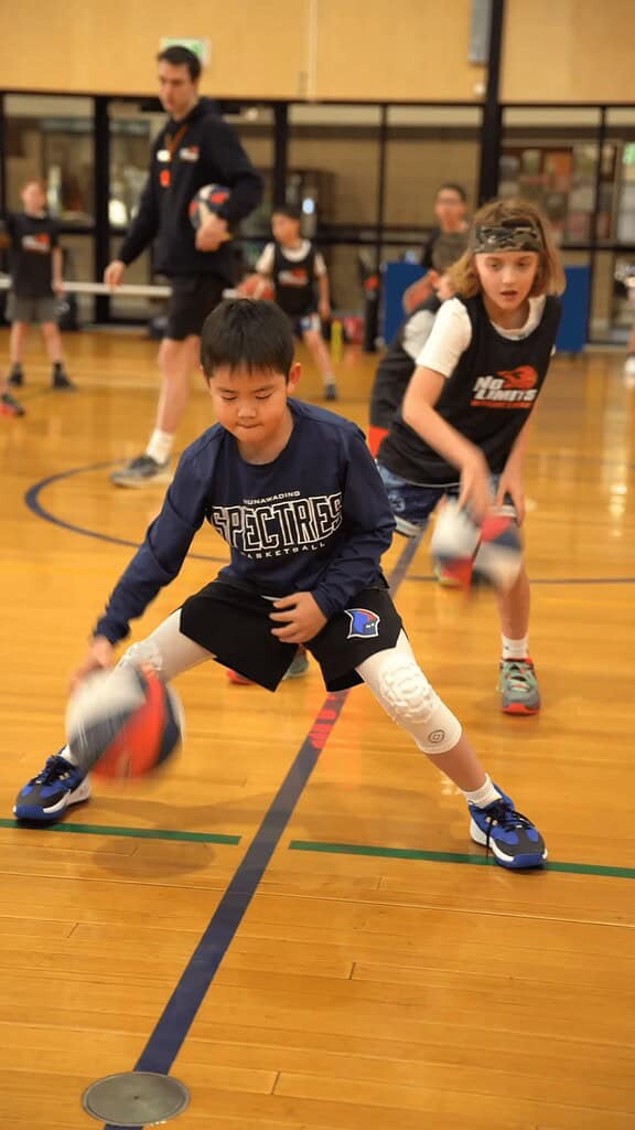 Young children practicing basketball drills in indoor gym.